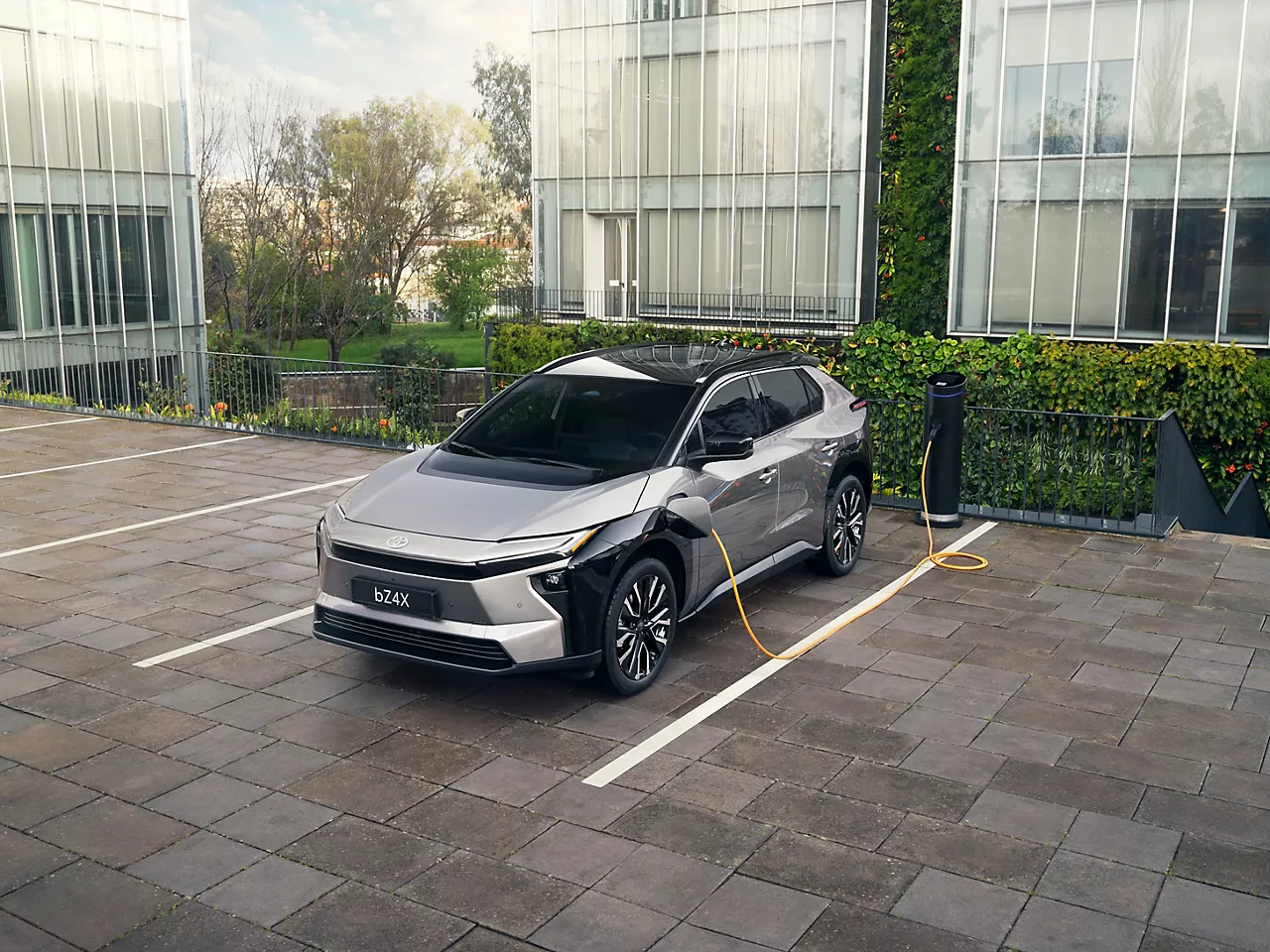 Ein bZ4X steht auf einem Dachparkplatz umrundet von Glasgebäuden und lädt dabei an einer Ladesäule